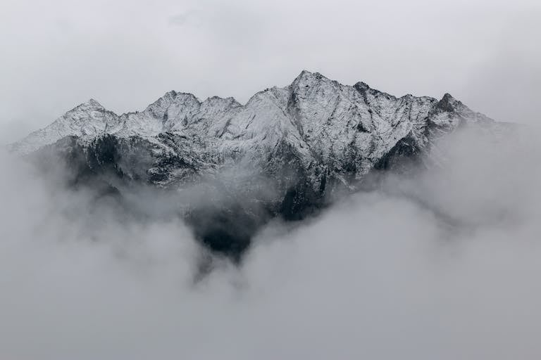 A breathtaking view of snow-covered mountain peaks surrounded by dense fog, creating a mystical landscape.
