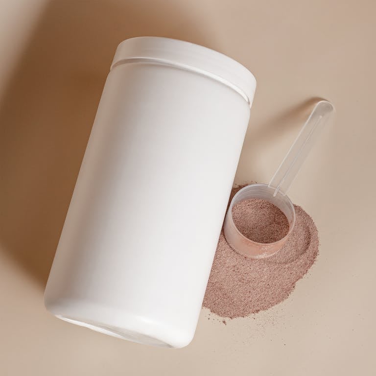 White container with cocoa powder spilling out and scoop lying next to it.